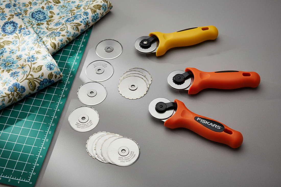 A yellow Driffy rotary cutter and two orange Fiskars cutters with loose 45mm straight and pinking blades laid out between them