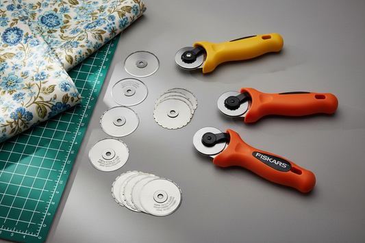 A yellow Driffy rotary cutter and two orange Fiskars cutters with loose 45mm straight and pinking blades laid out between them