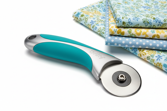A teal handled rotary cutter beside a folded stack of blue, green and yellow floral quilting cotton